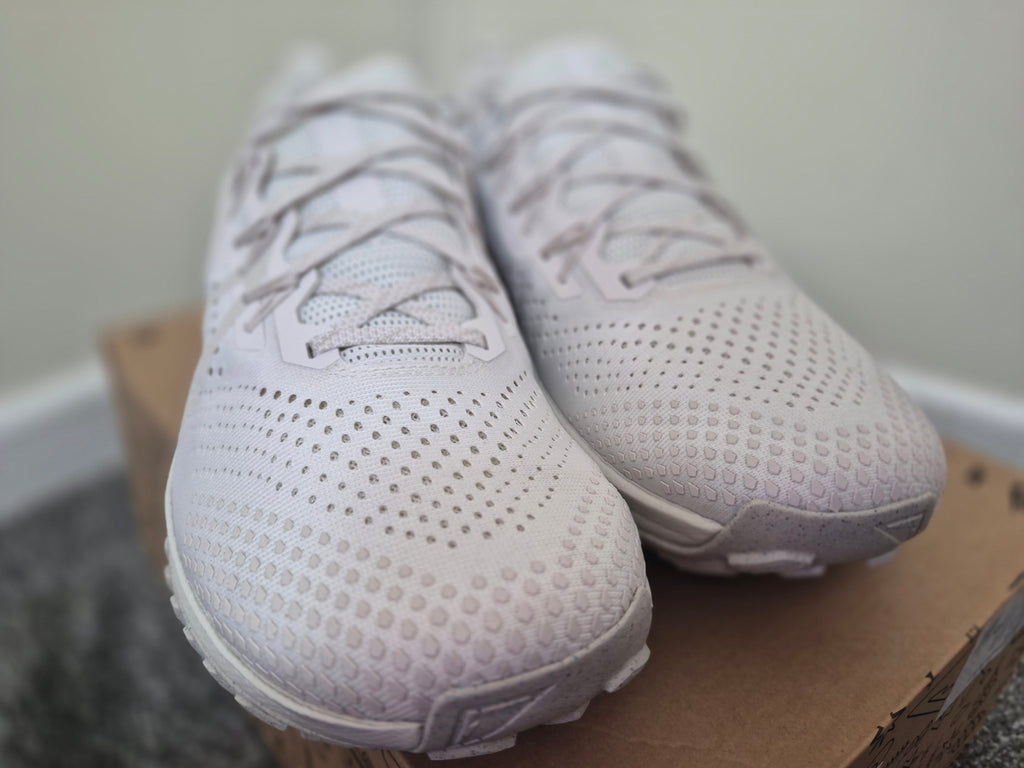 A pair of white knit athletic sneakers with a textured dotted pattern, in a front view.