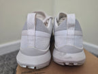 A pair of white and light gray athletic sneakers shown from the back, resting on a cardboard box against an indoor wall and floor background.