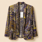A women's open-front blazer with a dense, intricate patchwork-style print in purple, gold, and beige, featuring a white product tag hanging from the collar.