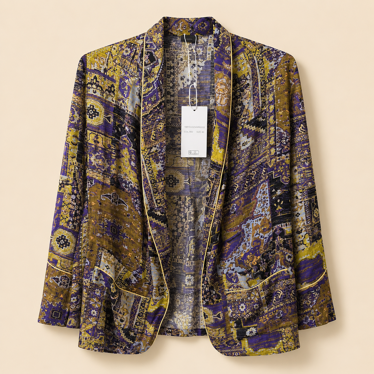 A women's open-front blazer with a dense, intricate patchwork-style print in purple, gold, and beige, featuring a white product tag hanging from the collar.
